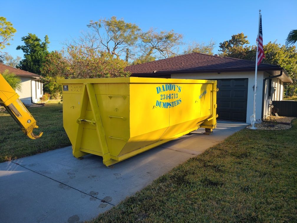 20-yard yellow dumpster in a driveway beside a house and garage, with a blue sky and trees in the background.