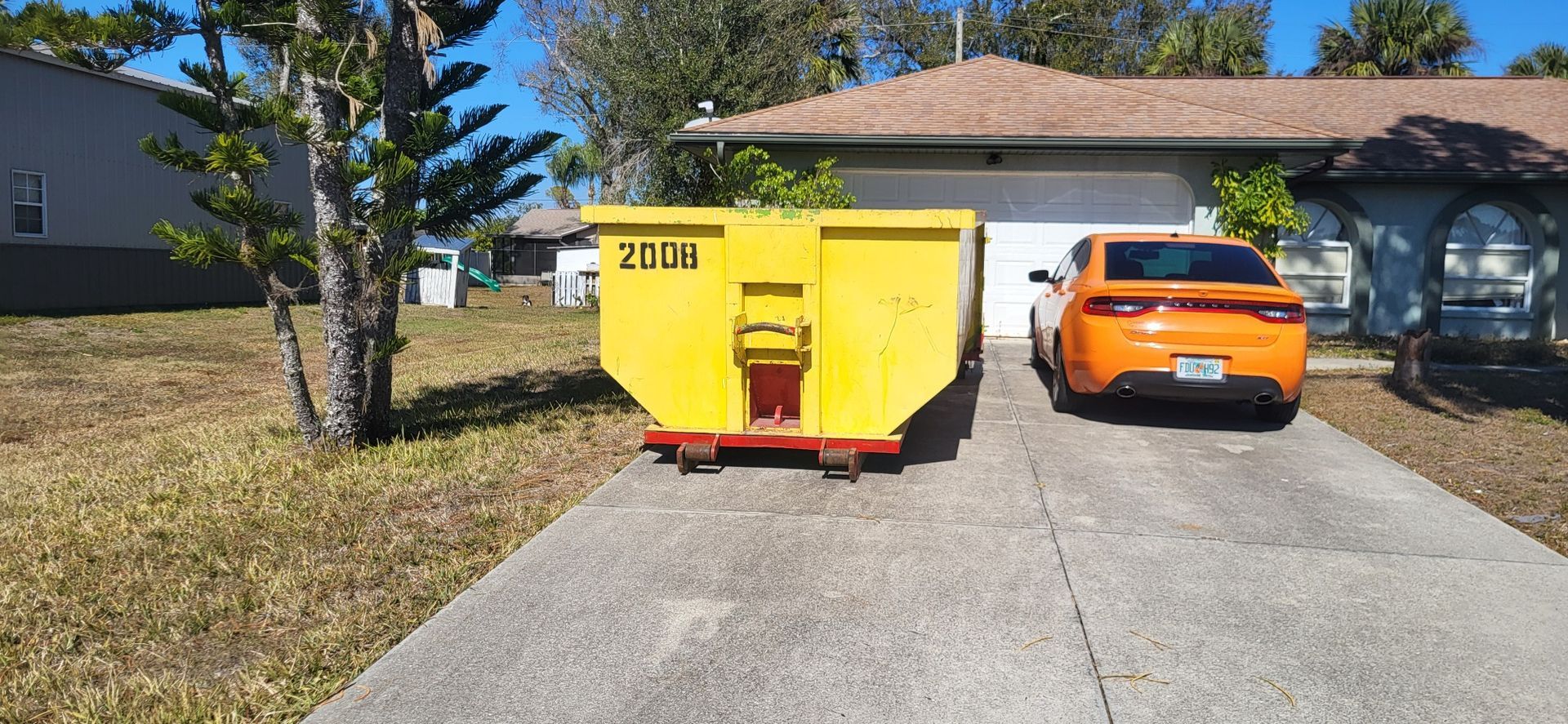 20-yard yellow dumpster and orange car parked in a driveway beside a house