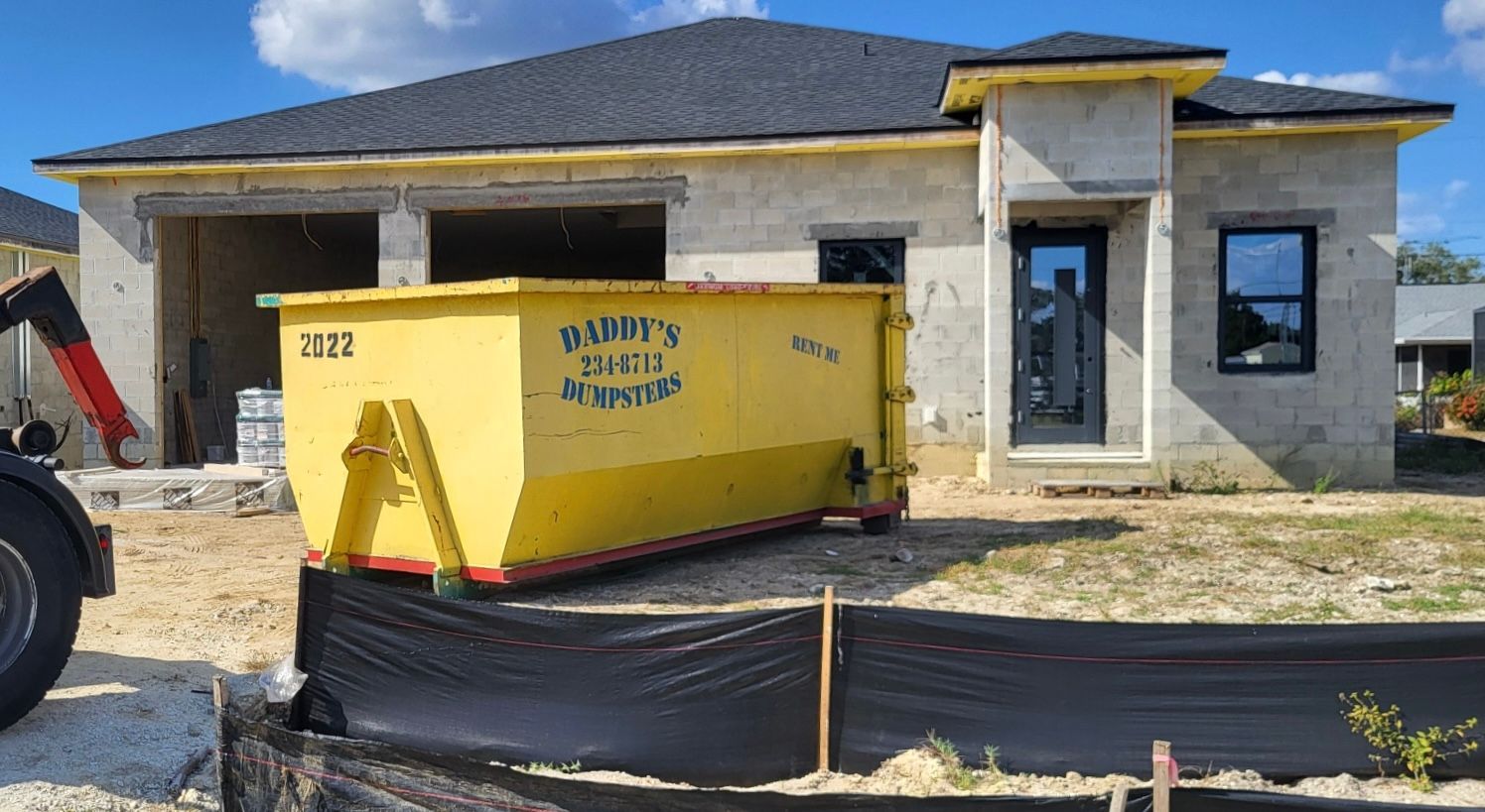 20-yard yellow construction dumpster in front of a newly built house with a dark roof and stone facade