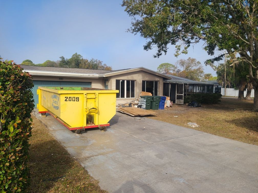20-yard yellow dumpster in a driveway beside a house, with roof repairs in progress.