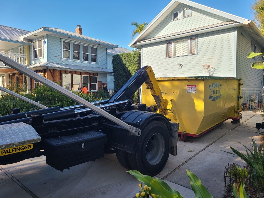 20-yard yellow dumpster on a driveway beside a black roll-off truck in a suburban neighborhood