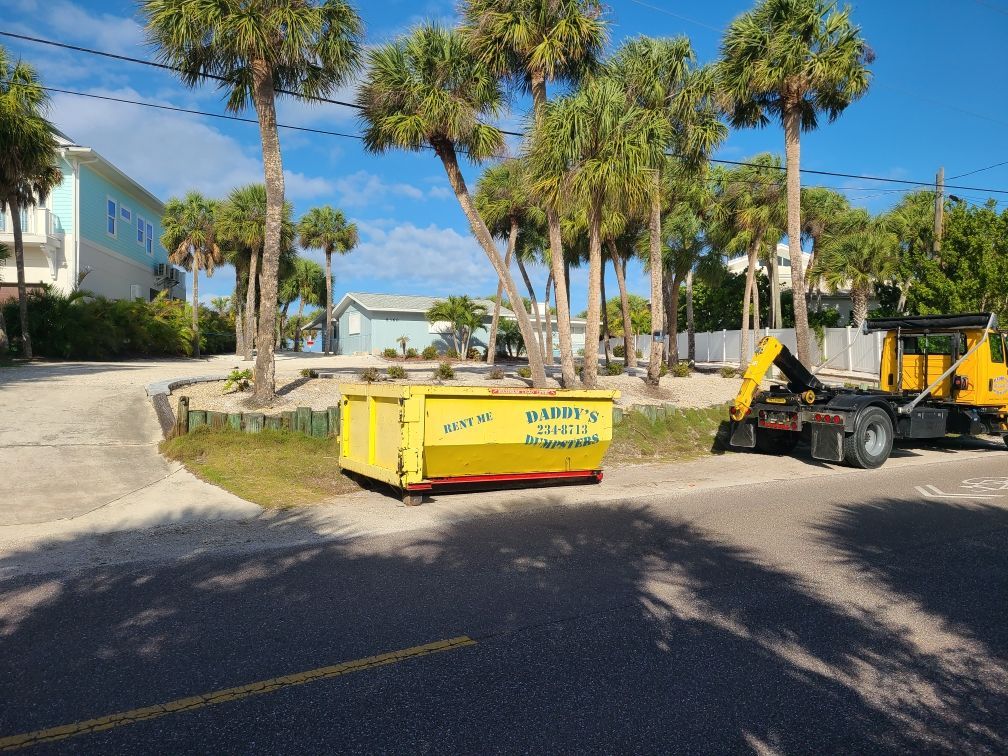 10-yard Yellow construction dumpster and equipment on a sunny street lined with palm trees.