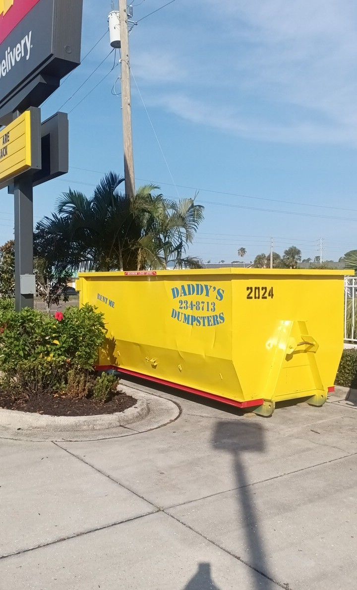 20-yard yellow dumpster on a sidewalk near a signpost, with blue lettering and red base trim.