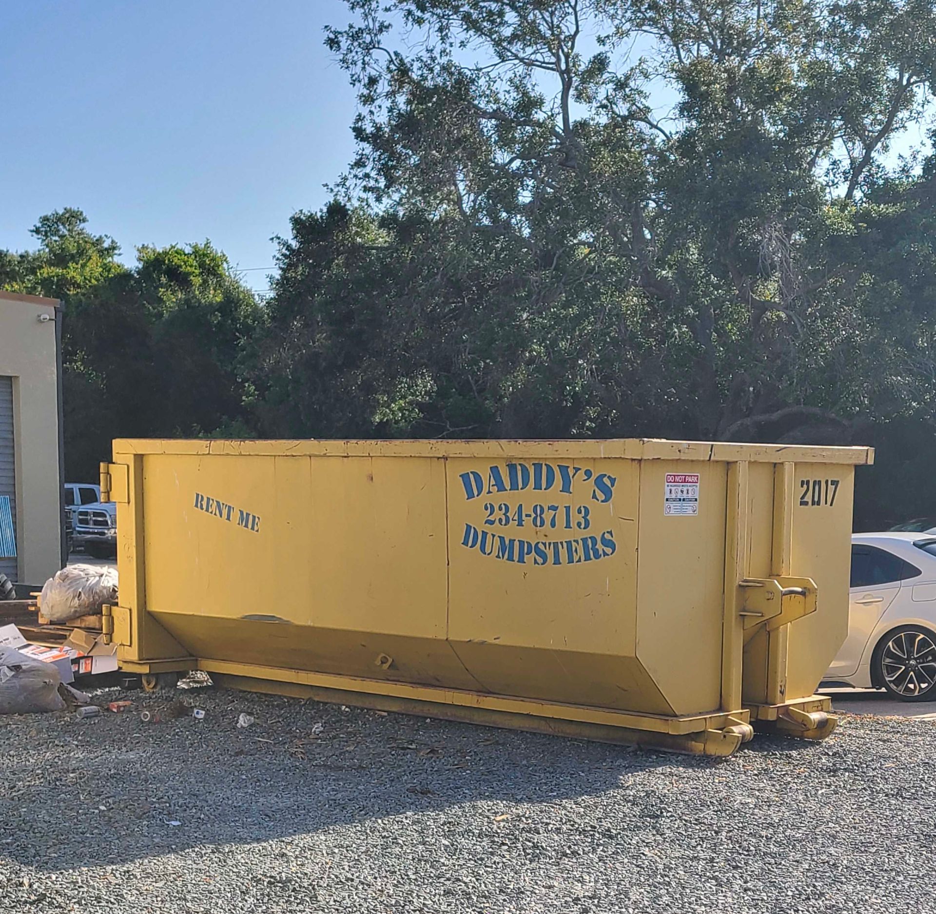20-yard yellow dumpster in a gravel lot, labeled “Davy’s Junk Dumpsters,” with trees and a building behind it.