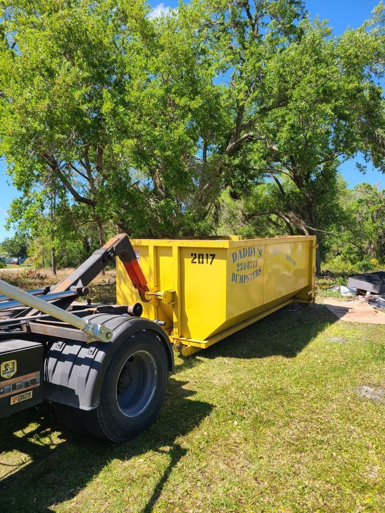 20-yard yellow roll-off dumpster beside a tow truck in a grassy yard under trees
