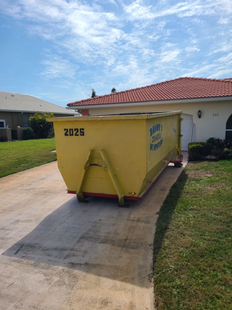 20-yard yellow dumpster on a driveway beside a house, with a red roof and blue sky overhead.