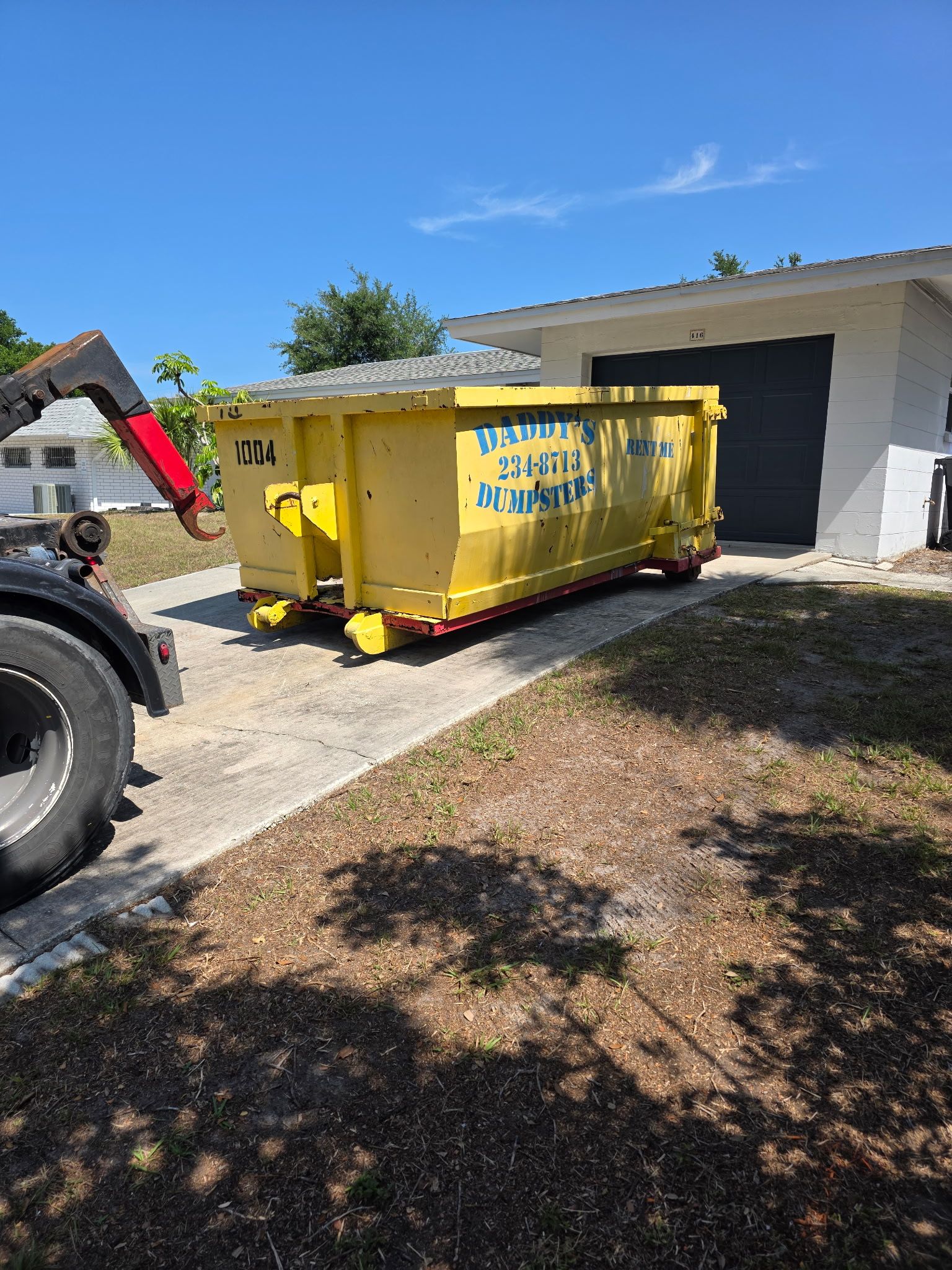 10-yard Yellow dumpster on a driveway beside a white house, with a tractor nearby under a clear blue sky