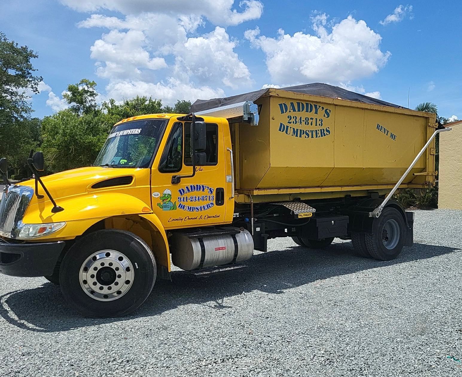 Yellow dump truck parked on gravel under a blue sky with clouds