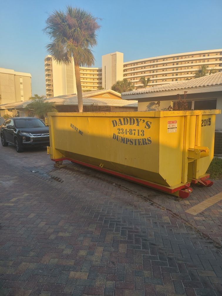 20-yard yellow dumpster in a paved parking lot beside a black car and apartment buildings at sunset
