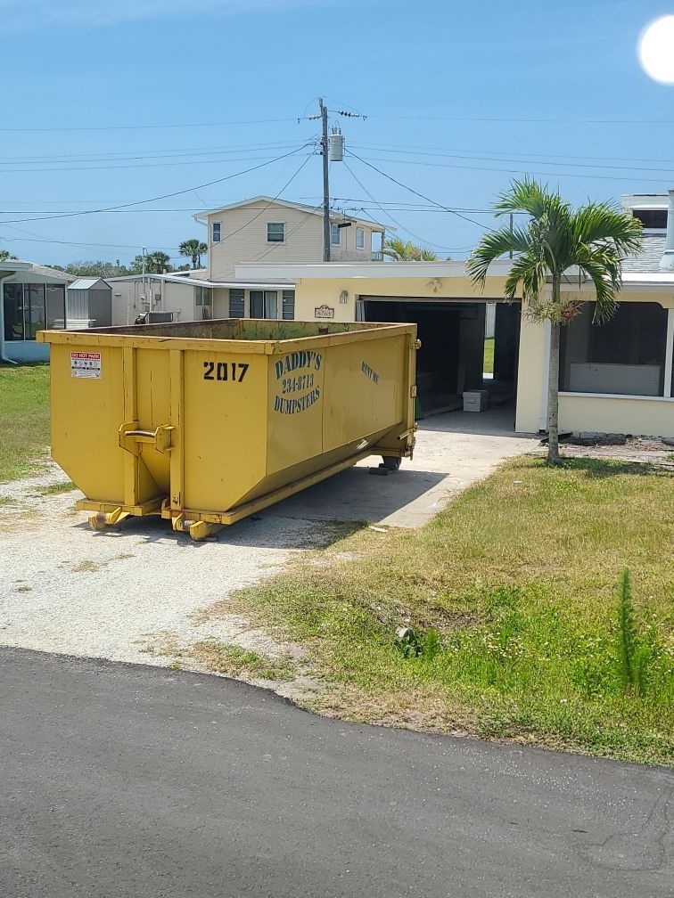 20-yard yellow dumpster in a driveway beside a suburban house on a sunny day.