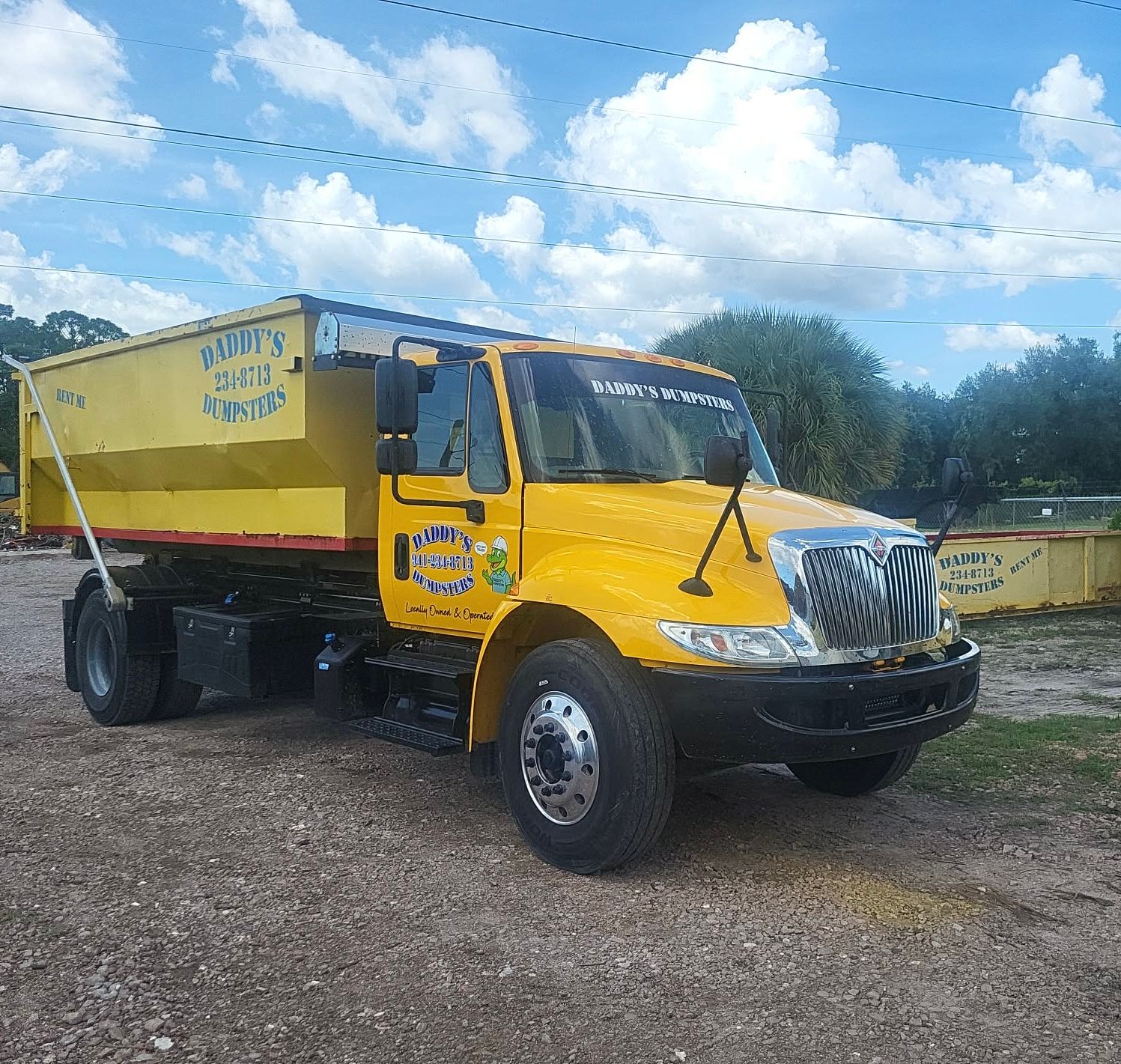 Yellow dump truck parked on gravel under a cloudy blue sky