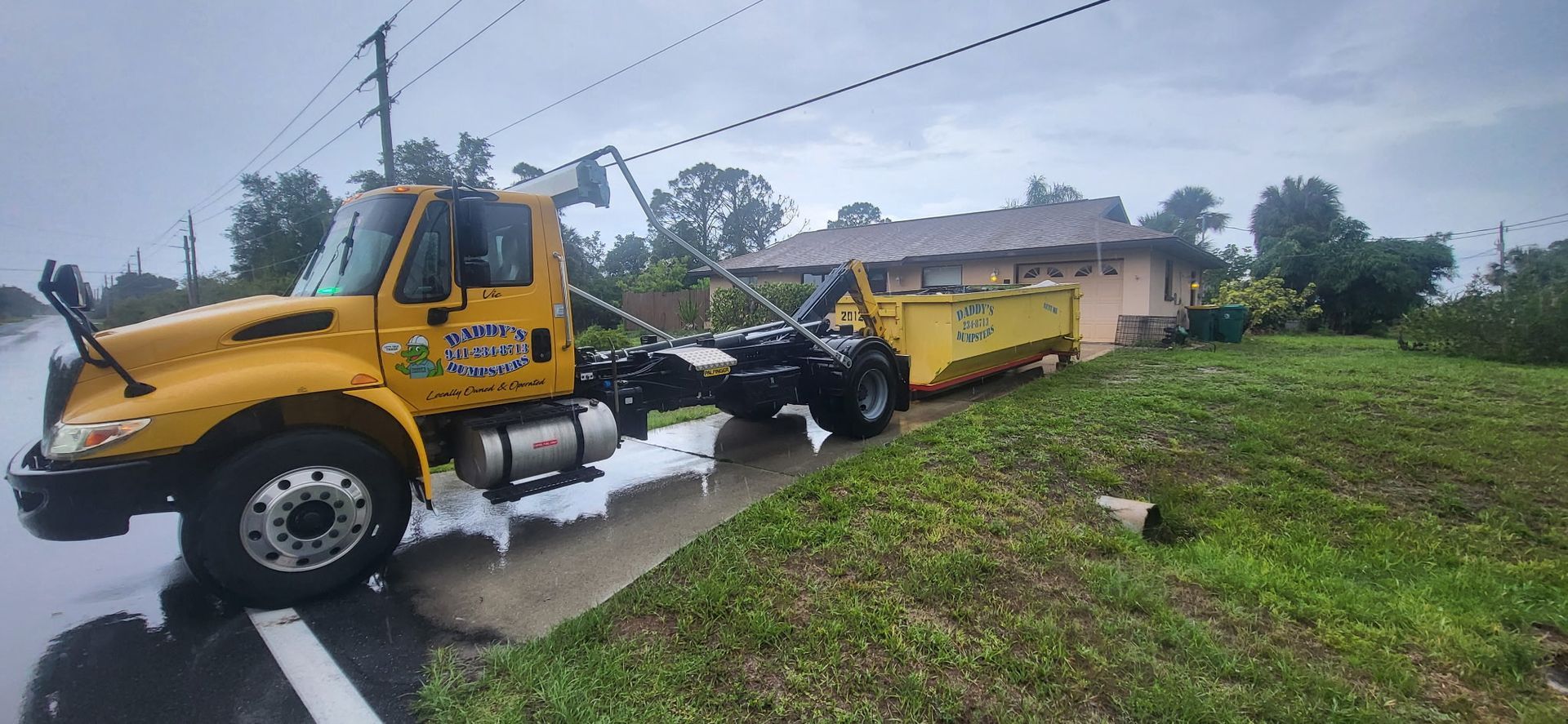 Yellow tow truck hauling a yellow dump trailer off a wet roadside into a grassy ditch