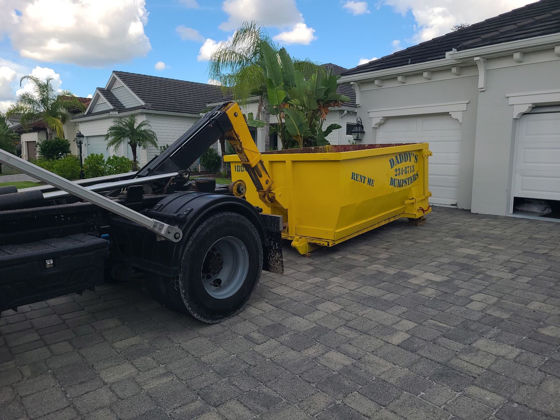 Yellow dumpster trailer parked in a driveway beside a white garage and house.