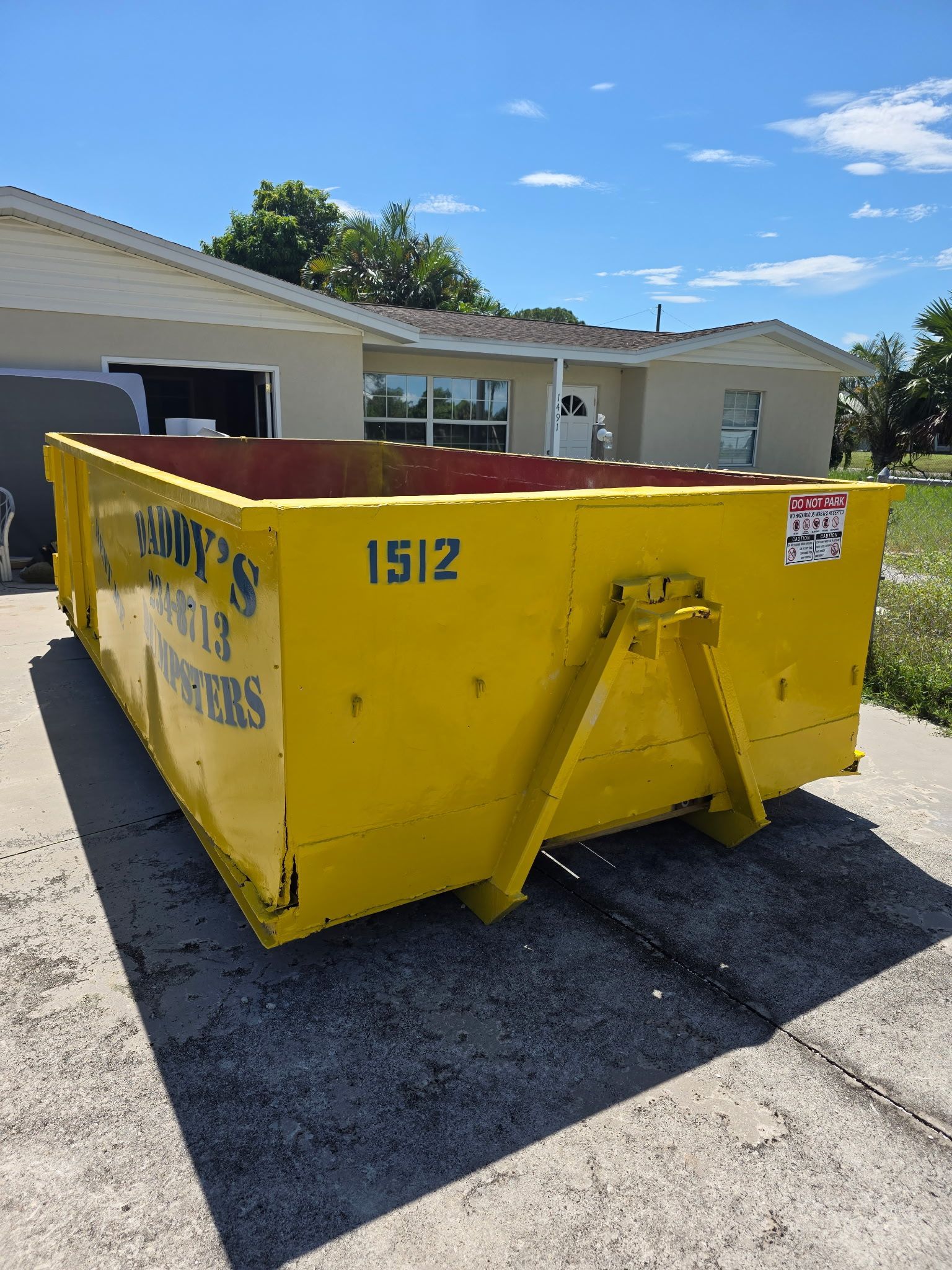 Yellow construction dumpster in a parking lot beside a beige building under a blue sky.
