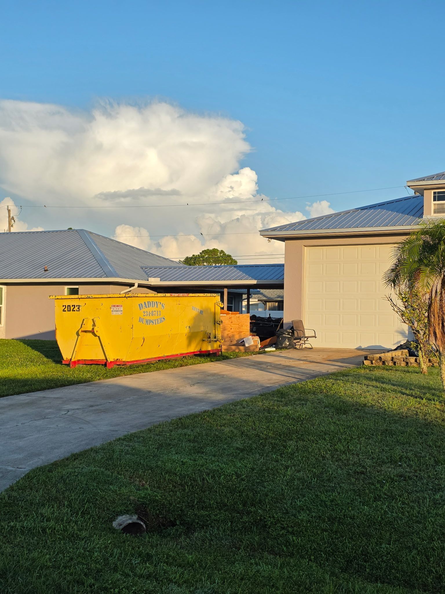 Backyard with yellow dumpster, green lawn, and houses under a cloudy sky