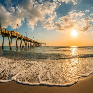 The sun is setting behind a pier in the ocean