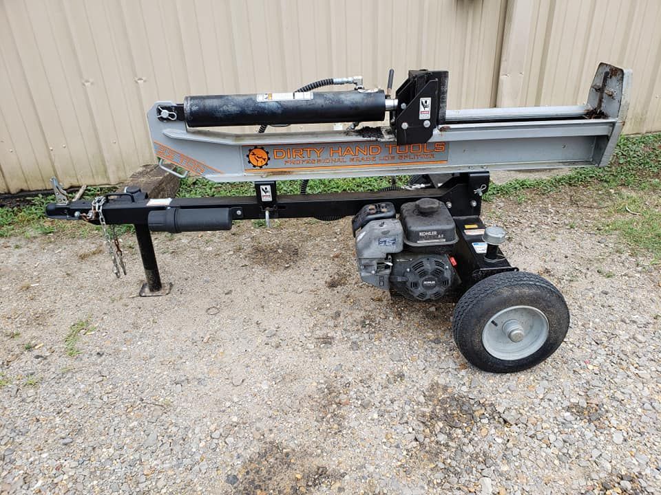 A log splitter is sitting on a trailer on a gravel road.