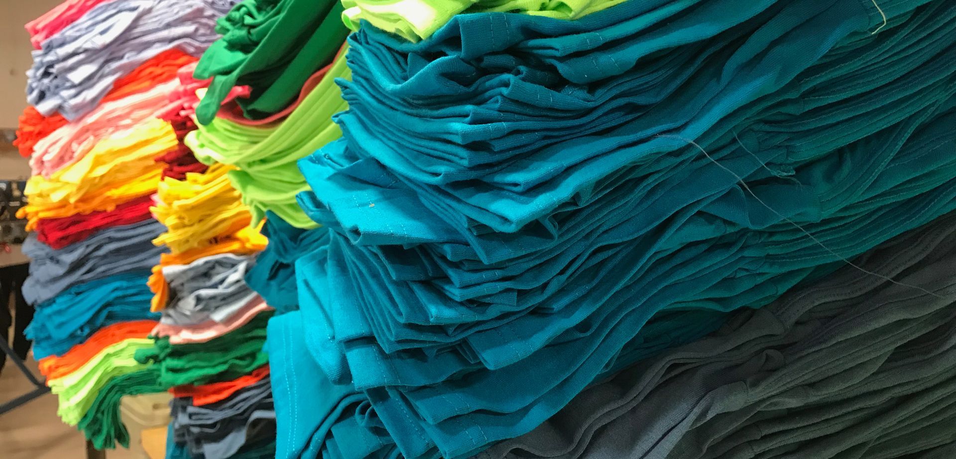 A bunch of colorful t-shirts are stacked on top of each other.