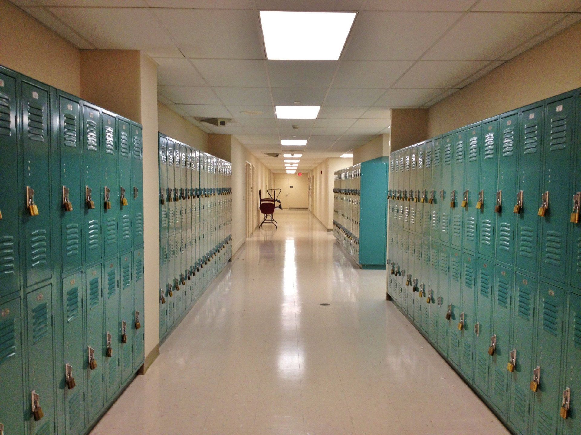 Hallway with rows of teal lockers, bright overhead lights, and a white floor.