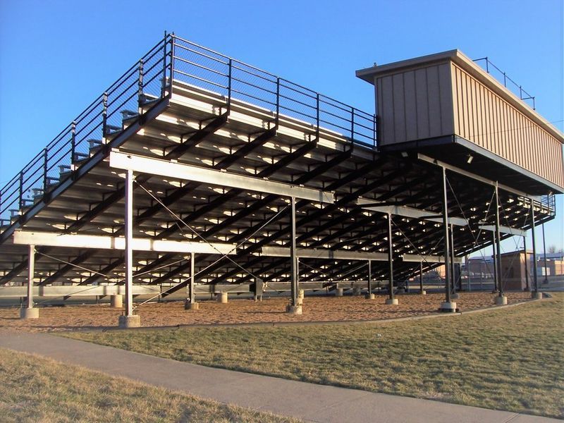 Bleachers and press box at a sports field on a sunny day. Brown and gray structure, blue sky.
