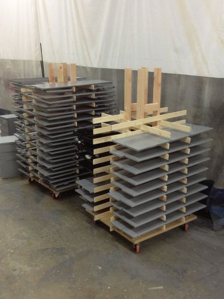 Two stacks of gray tiles on wheeled pallets with wooden supports, indoors.