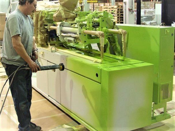 Man sprays green paint on industrial machine.