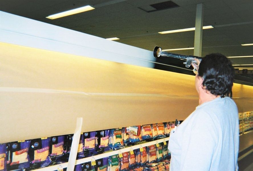Person spraying cleaning solution on a long shelf in a grocery store.