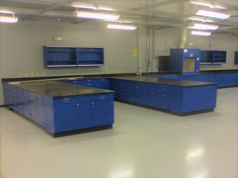 Empty blue lab with countertops and cabinets, fluorescent lighting, and grey walls.