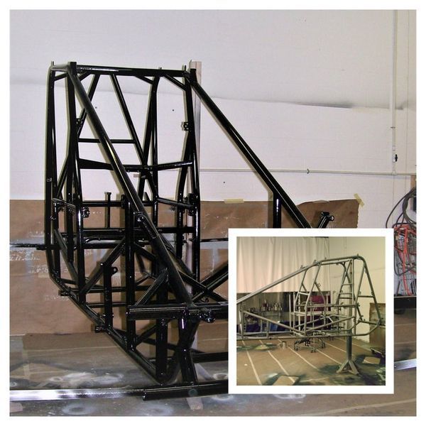 Black tubular steel vehicle chassis, with inset of unfinished chassis in workshop.