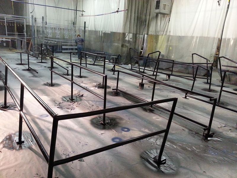 Black metal guardrails bolted to a concrete floor. A person stands in the background. Industrial setting.