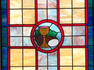 stained glass window depicting a chalice, grapes, and a loaf of bread, in a red-framed circle, centered