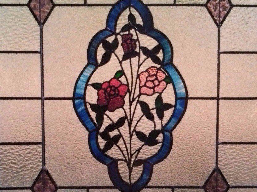 stained glass window with central floral design of pink and red roses, blue outline, and neutral background