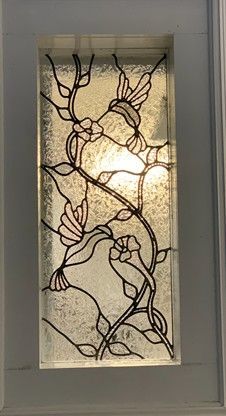stained glass panel: floral design with hummingbirds, black outlines, and textured glass, set in a white door