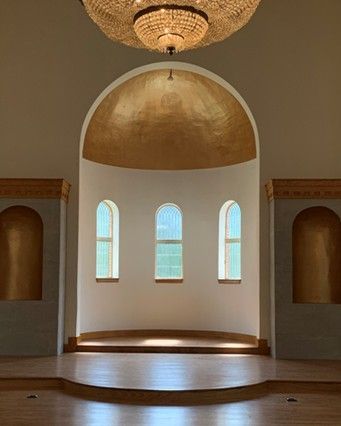 interior of a building with arched window and golden alcoves, sunlight streams in