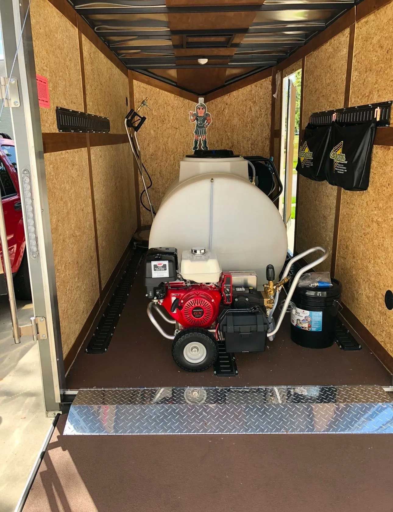 Pressure washing equipment inside a utility trailer. Red engine, white water tank, and black hoses are visible.