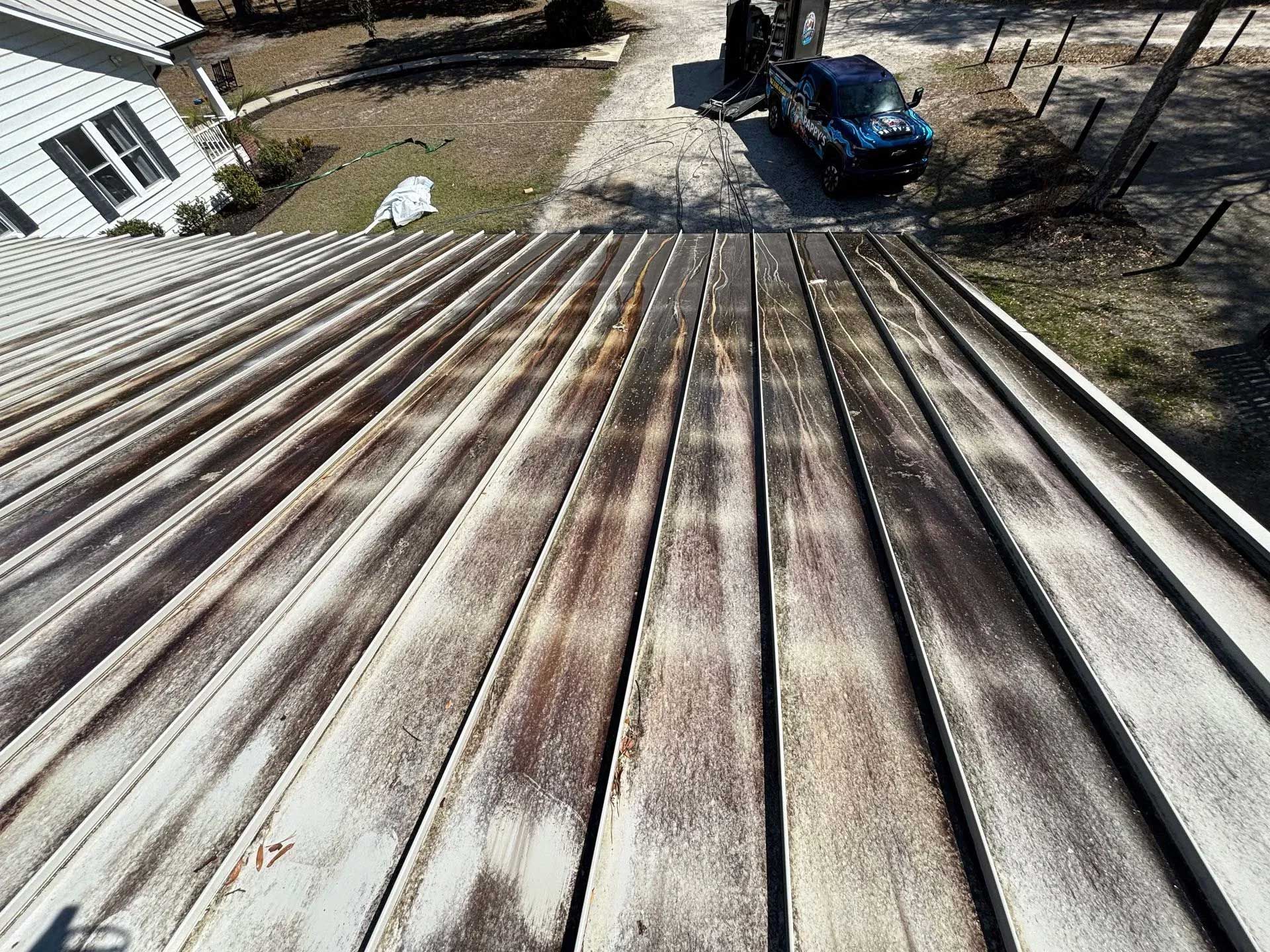 Metal roof with streaks of brown discoloration, outdoors with a driveway and a vehicle visible.