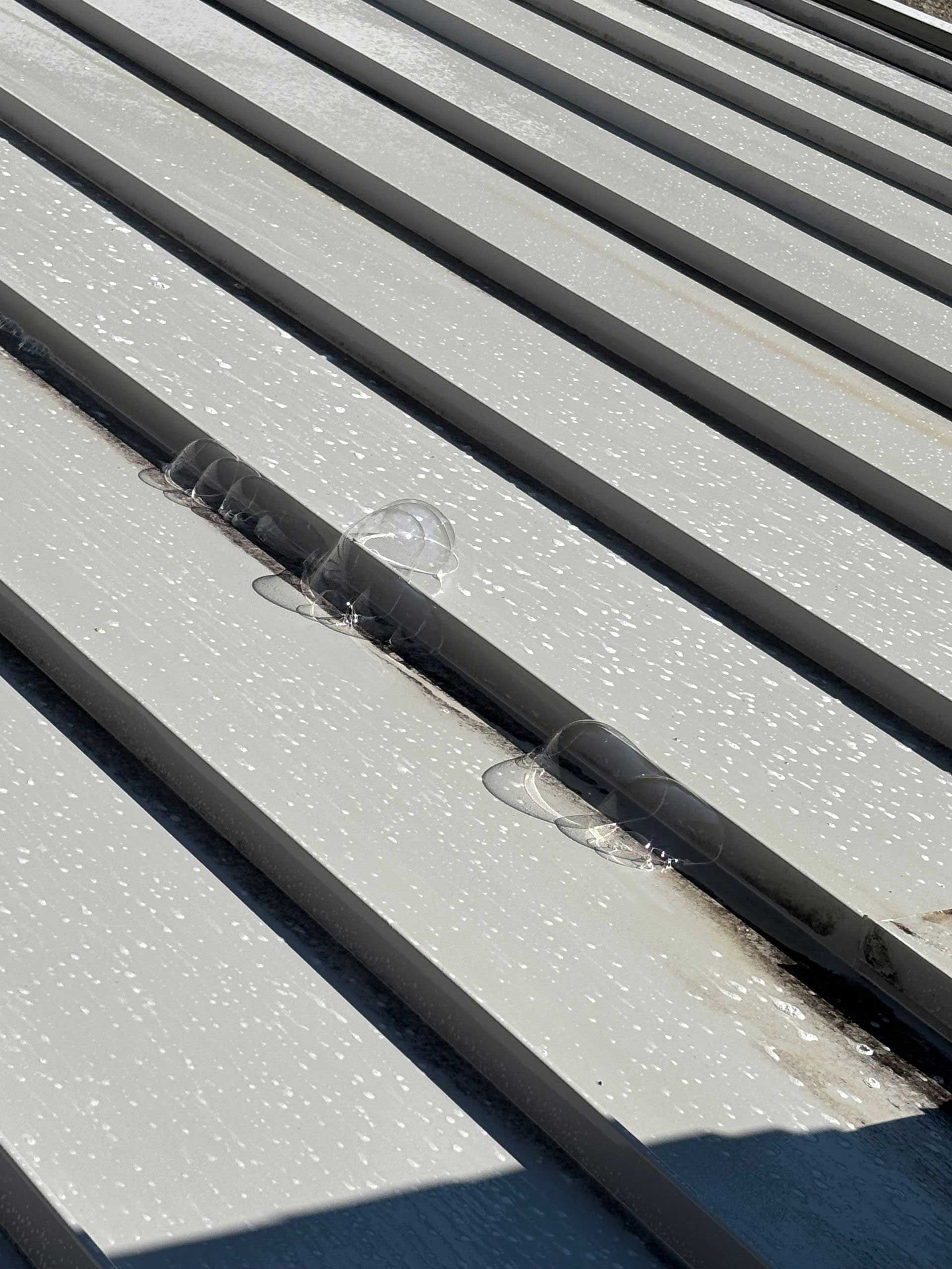 Close-up of a light-colored metal roof with a few water droplets collected in the groove.