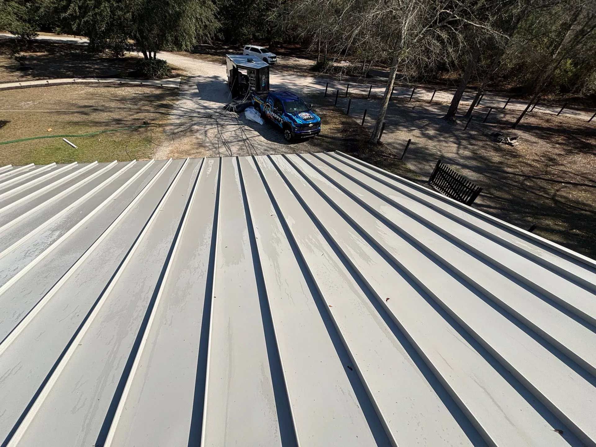 Gray metal roof, with a view of a driveway and vehicle in the background. Sunny day.