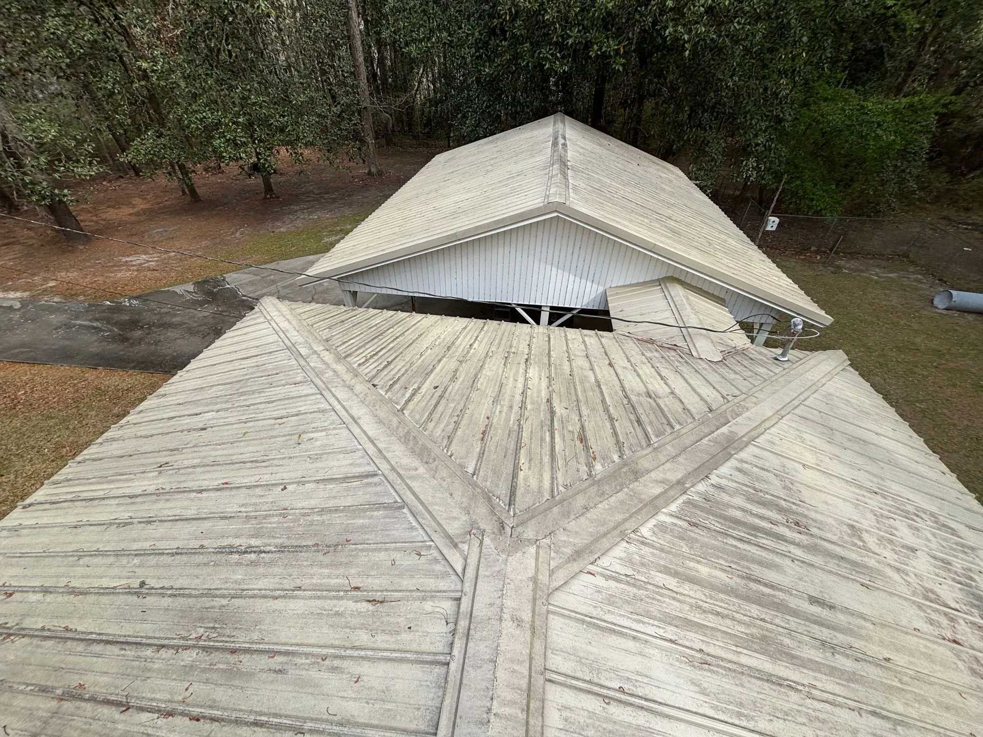 Two white, weathered gable roofs with a forested background.