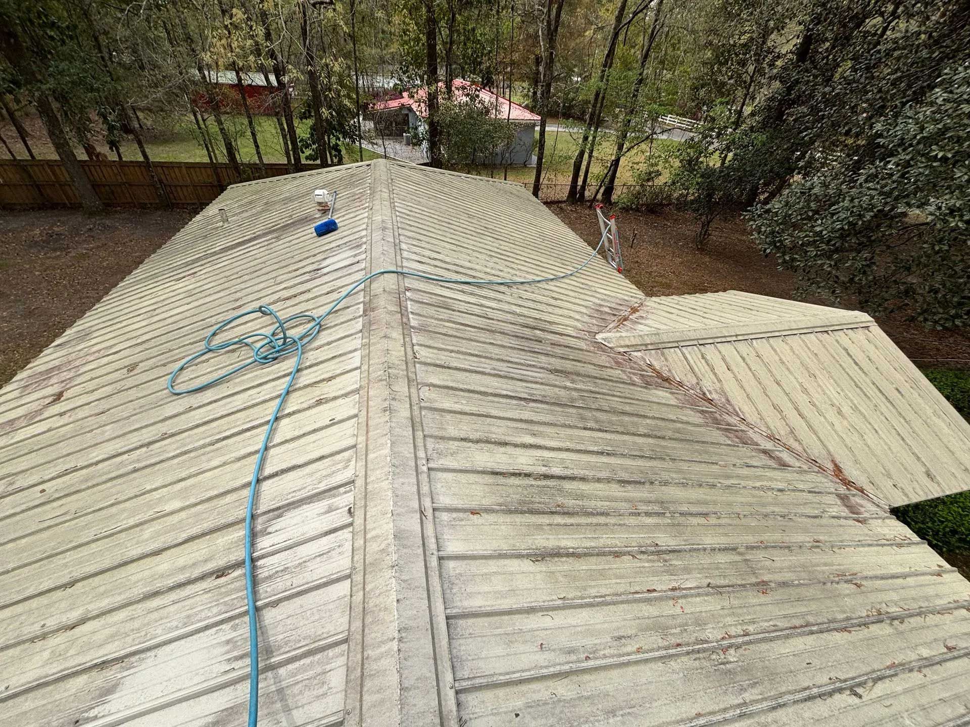 View of a light-colored metal roof. A blue hose lies across it with a person visible towards the top.