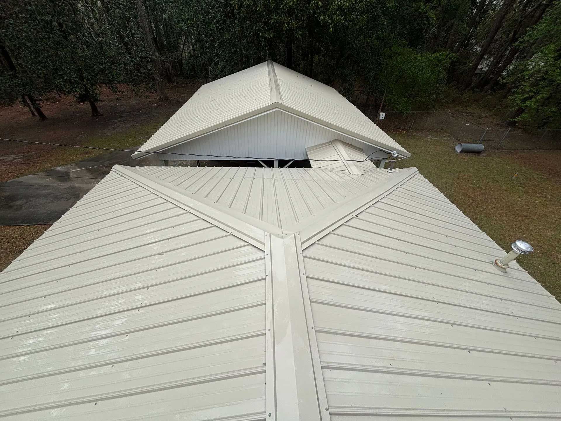 Overhead view of a white metal roof on a building with a grassy and wooded background.