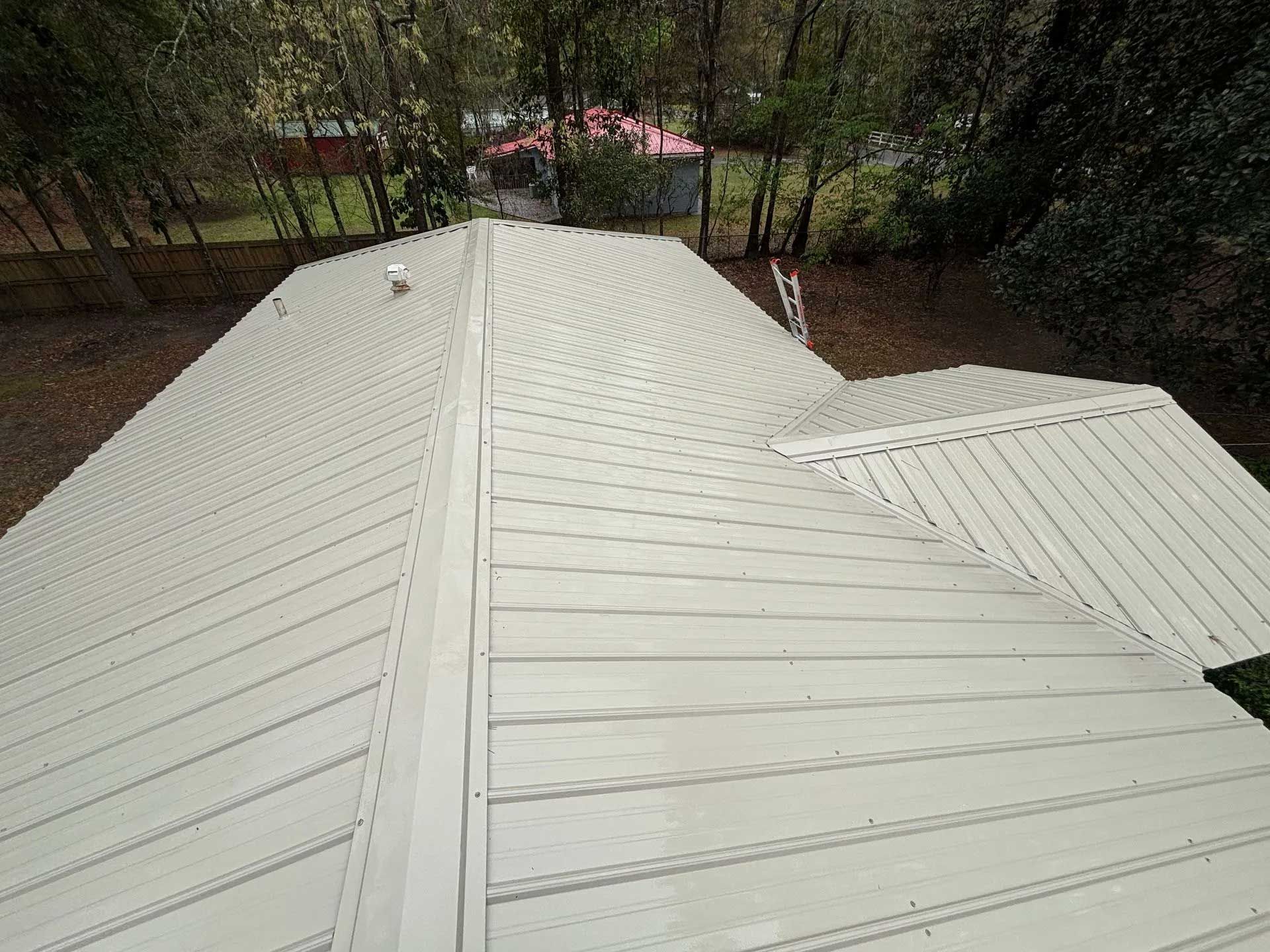 Overhead view of a light-colored metal roof on a house, surrounded by trees.
