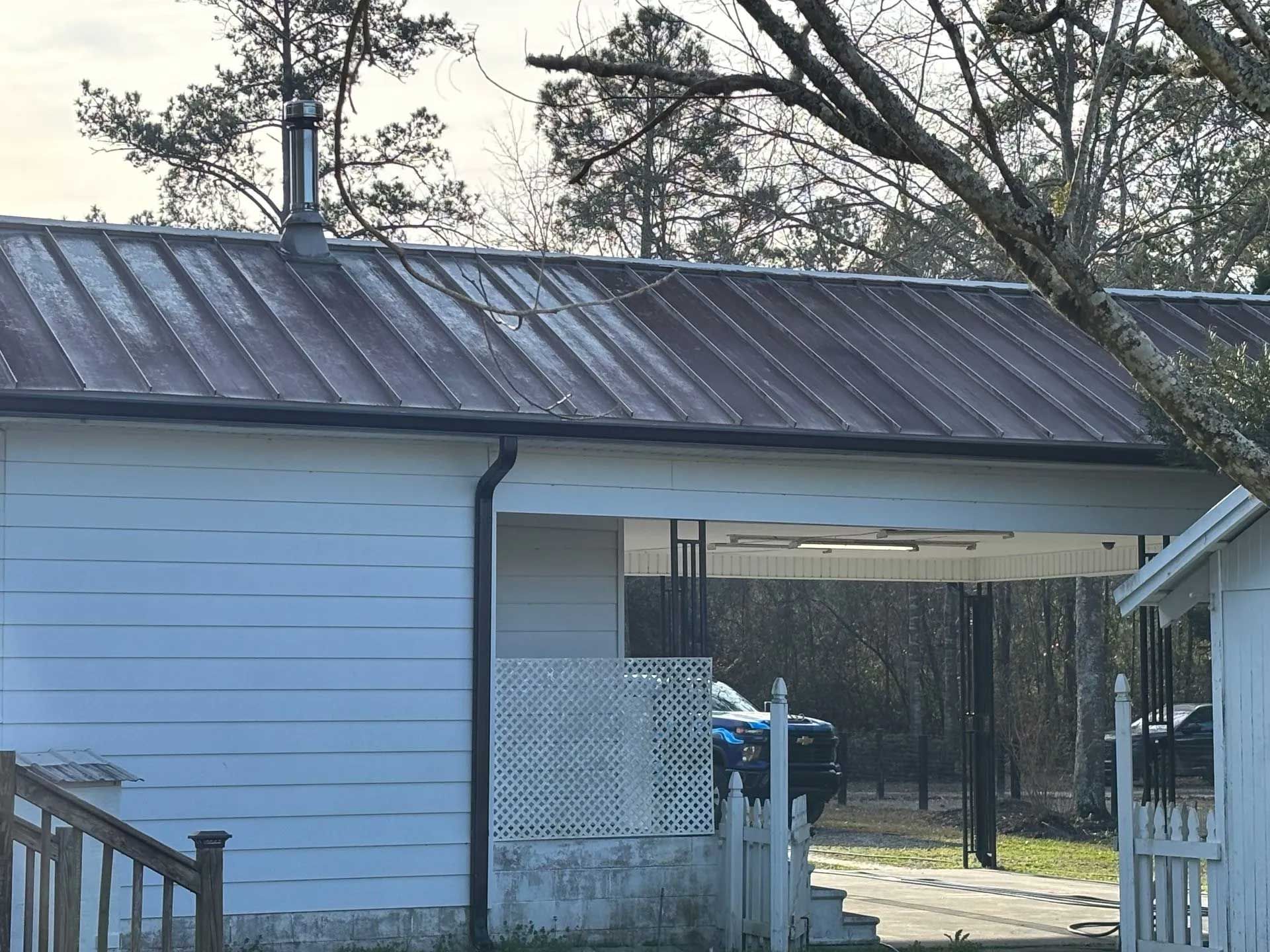 Metal roof on a white building, with a carport. Black gutter and chimney.