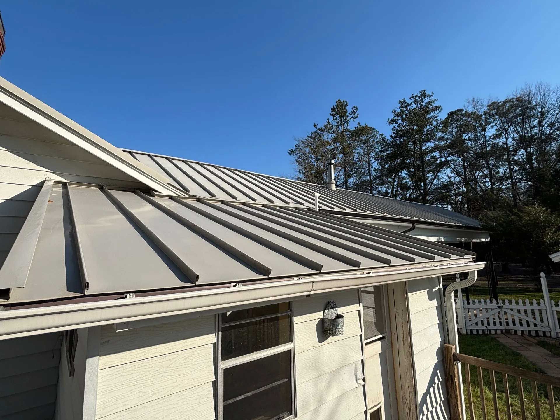 Gray metal roof on a white house with a blue sky background.