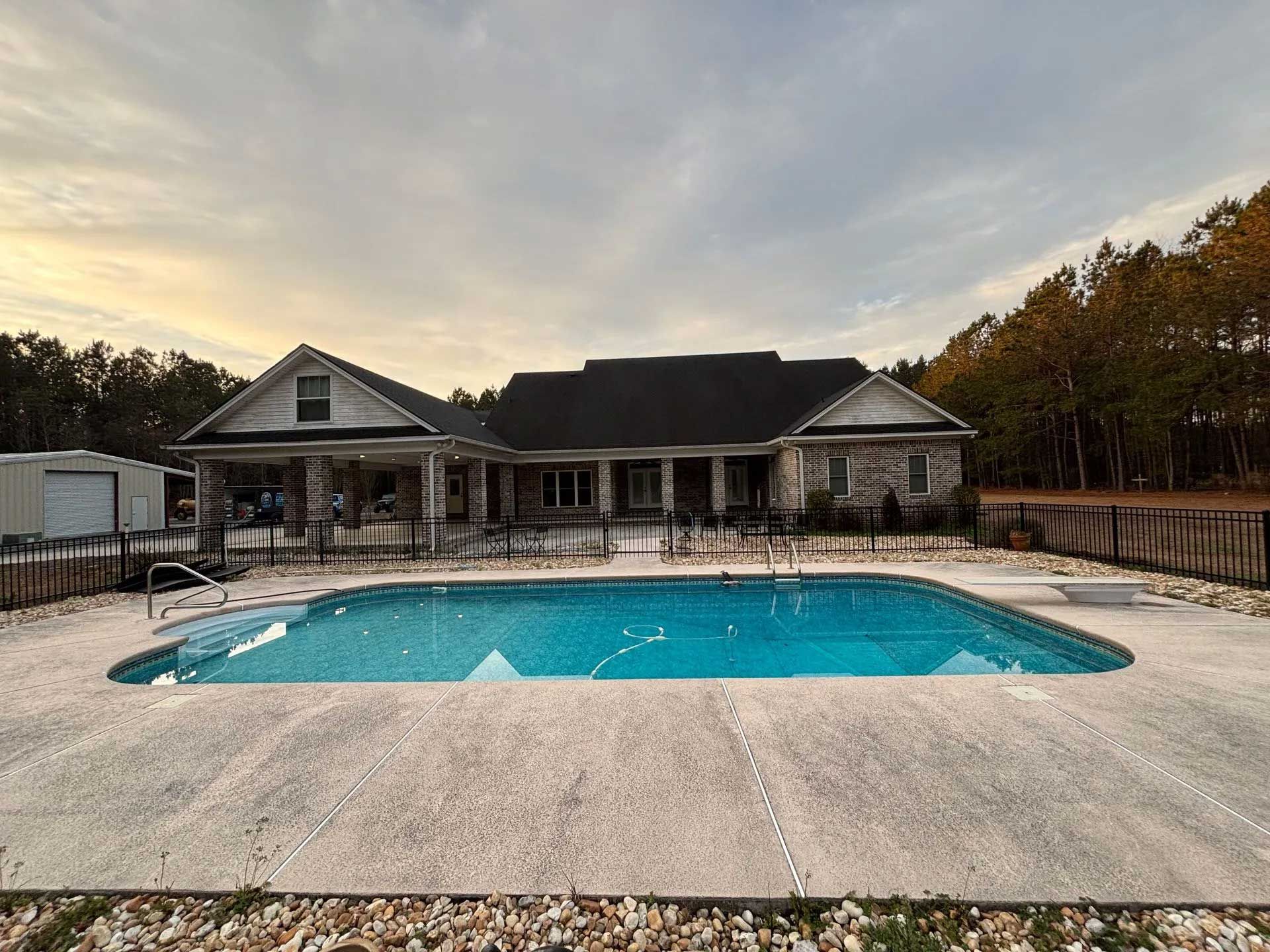 Swimming pool in front of a house, under a cloudy sky. Trees and a small shed in the background.
