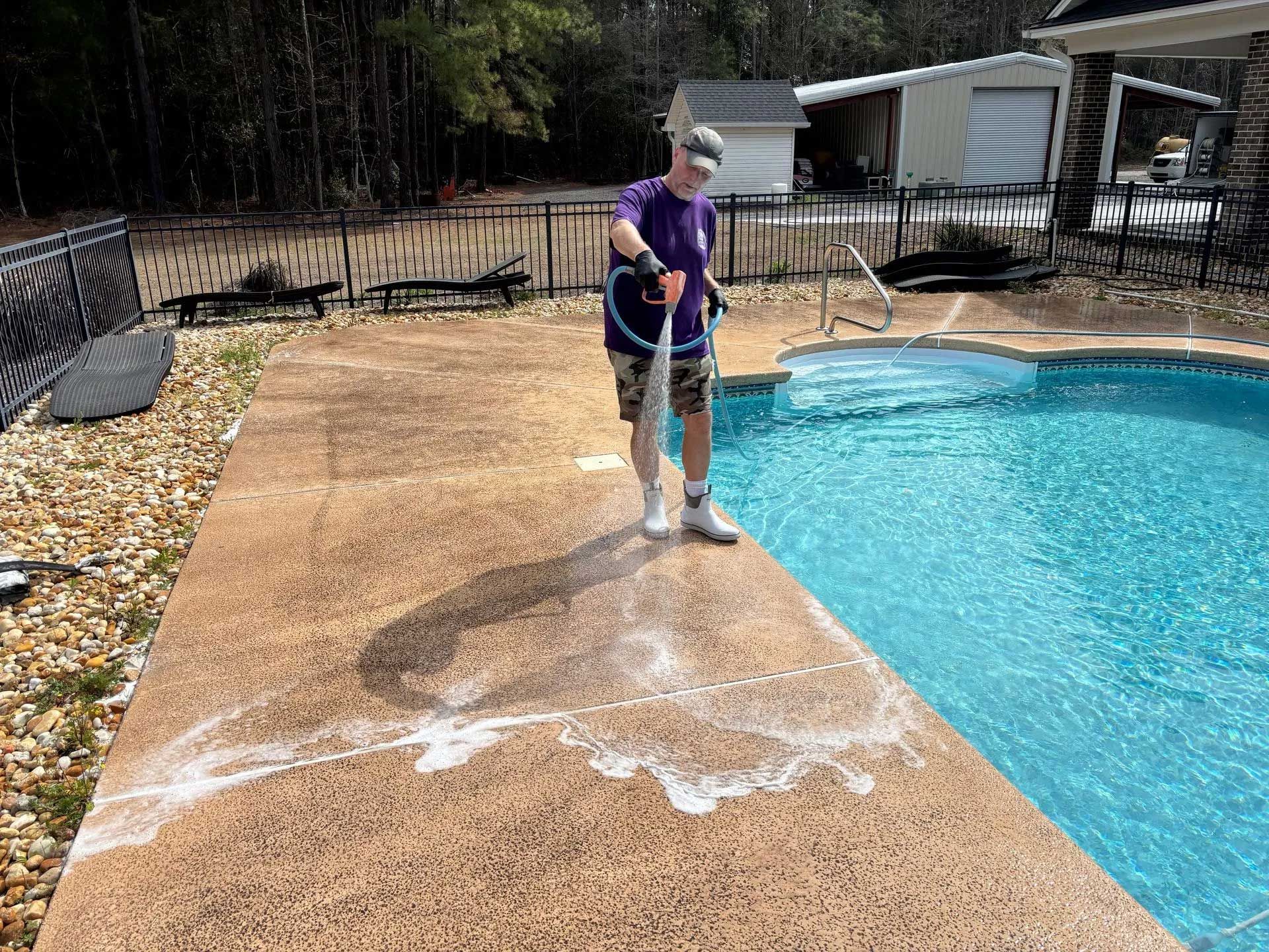 Person spraying soapy water on a pool deck next to a pool.