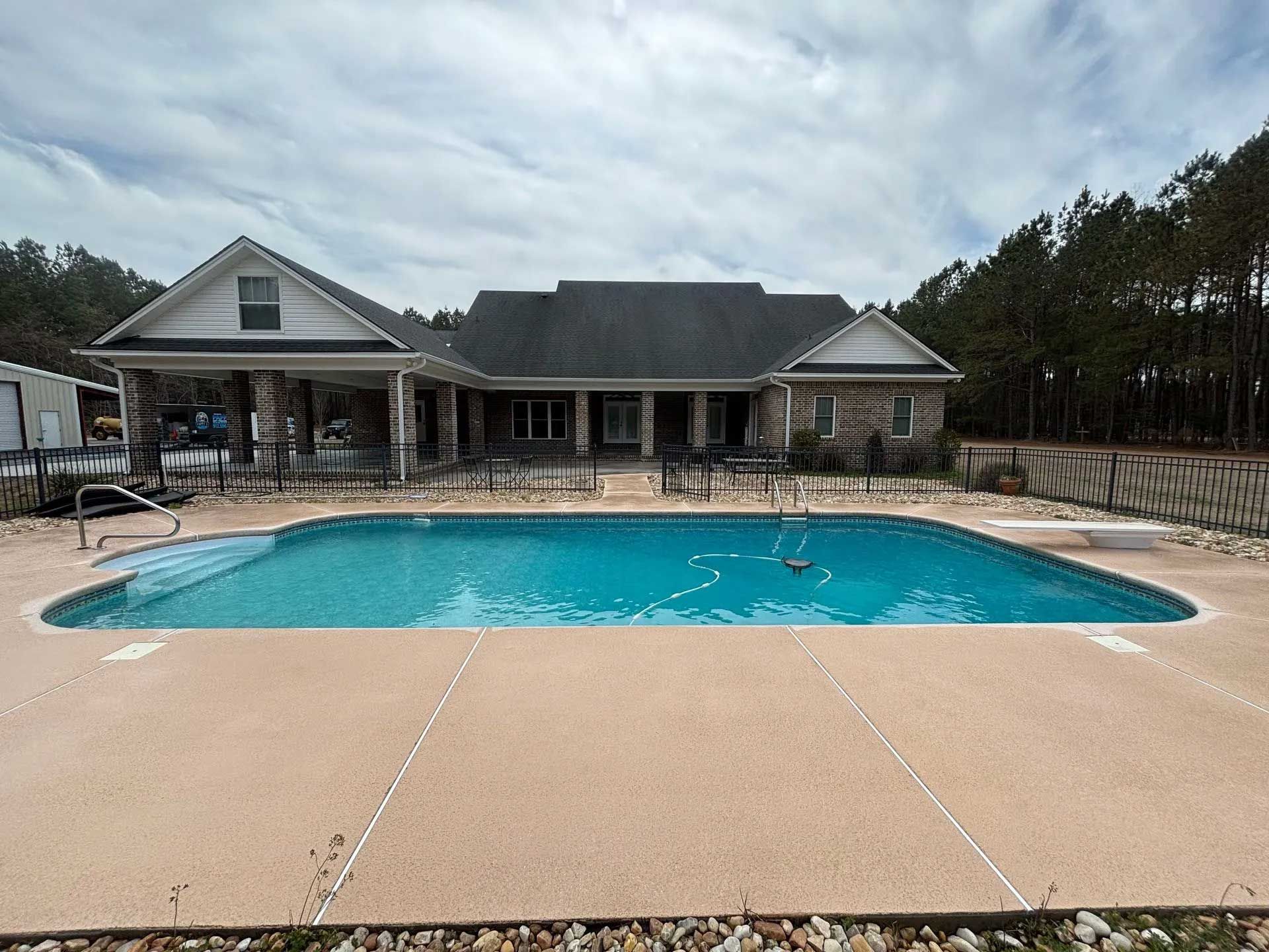 A swimming pool in front of a house with a stone facade, under a cloudy sky.
