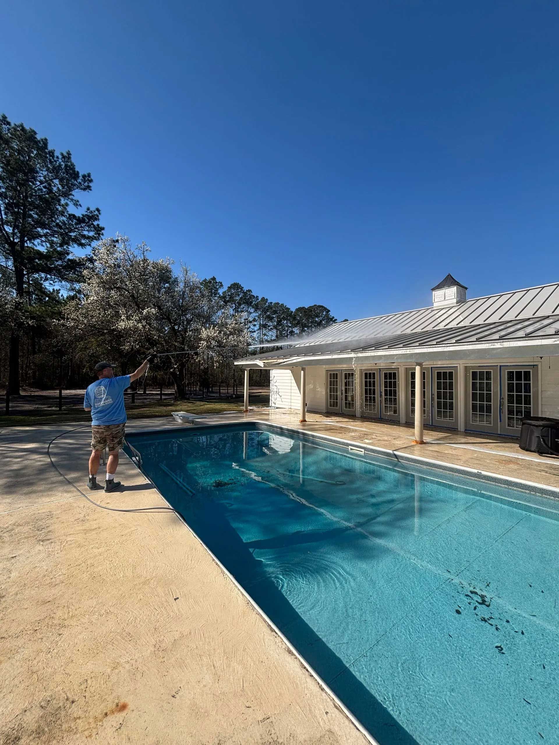 A man stands beside a rectangular pool in front of a white house with a metal roof.