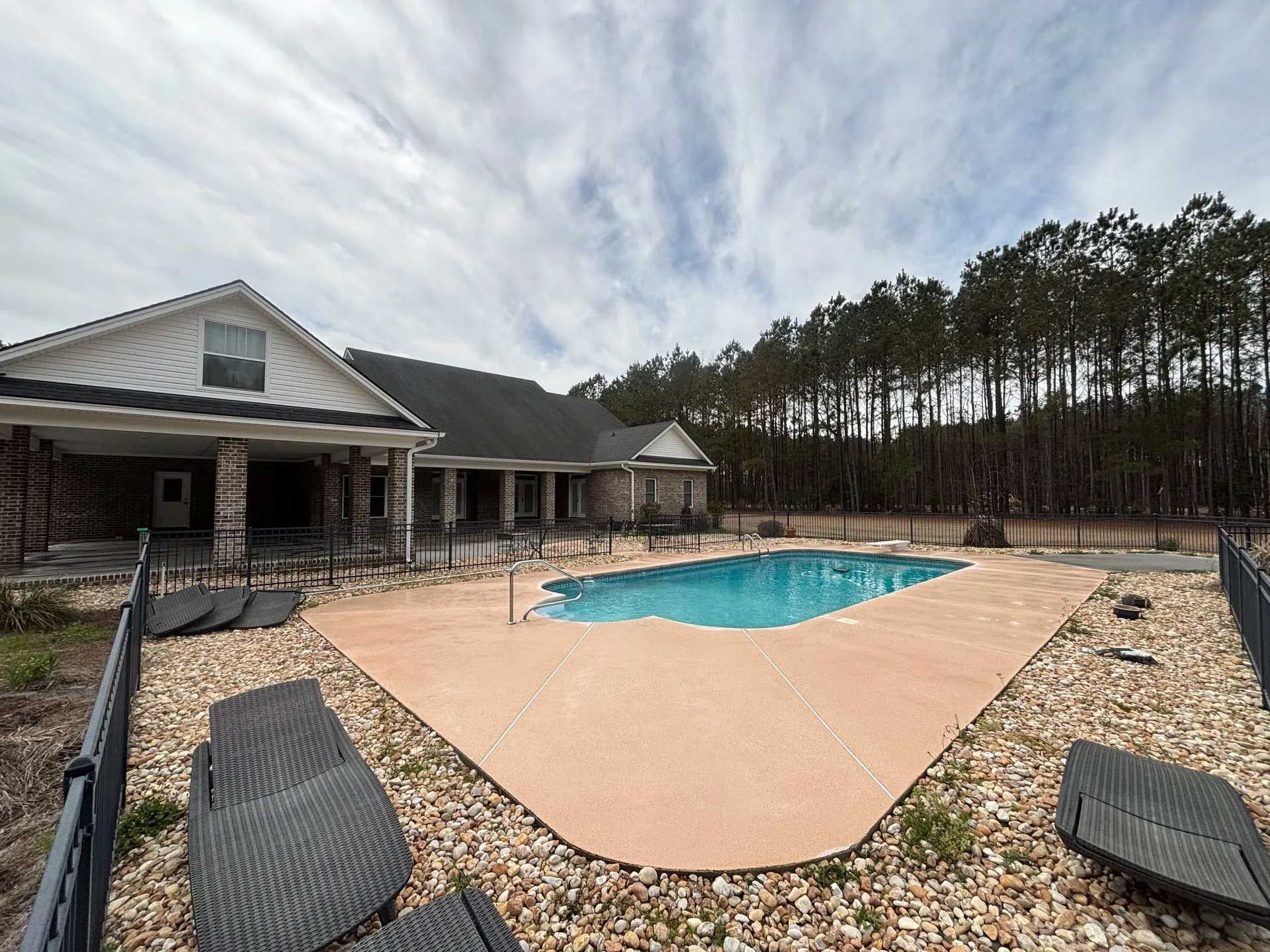 A house with a pool in the backyard. The pool has a concrete deck and a black fence.