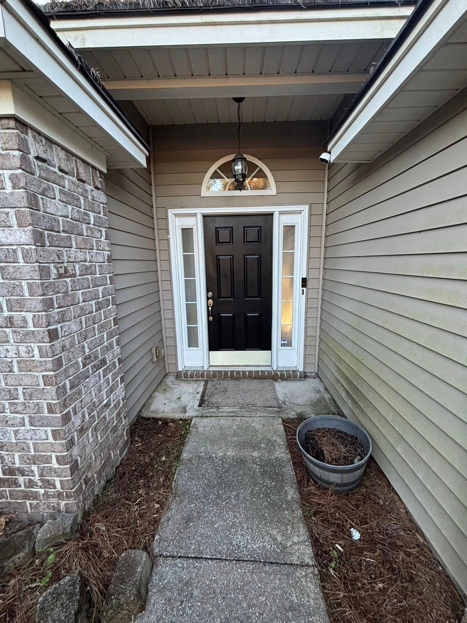 A black front door with side windows and an arched light fixture, situated at the end of a stone path between siding walls.